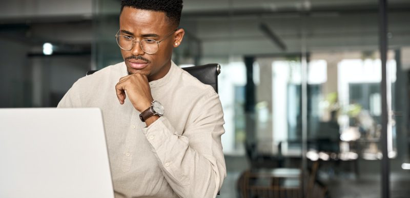 Busy African business man thinking on online investment working on laptop.