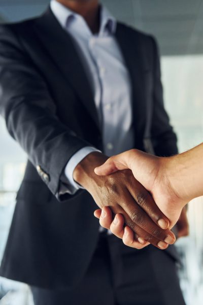 Doing handshake with customer. Young african american businessman in black suit is indoors